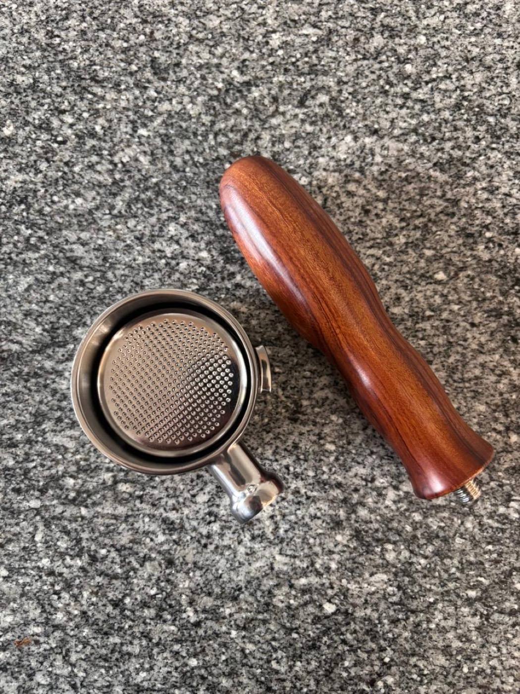 A bottomless THW portafilter with wooden handle and a precision basket on a granite counter